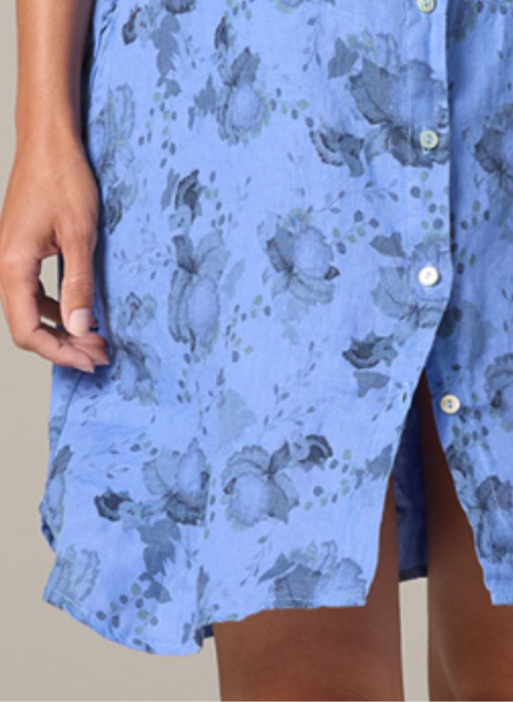 Linen Shirt Dress, shown in Forget me Not (periwinkle blue), size Small on 5’9” model.  Worn buttoned, with long sleeves rolled up.  Zoomed in to show the rounded shirttail hemline that is shorter on the sides, small white shell buttons, and washed floral print. 100% Linen, floral print.  Pre-shrunk, Machine washable, Made in the USA, by Cut Loose.